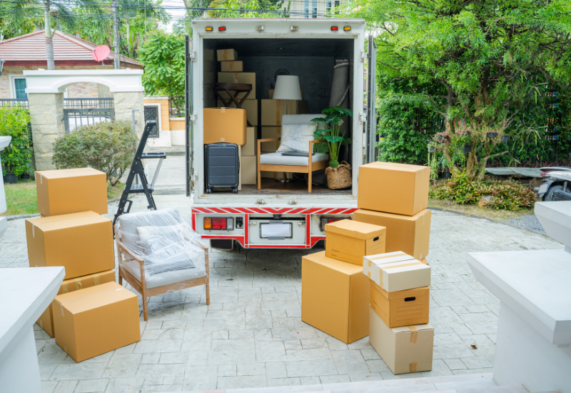 A moving truck filled with boxes and furniture is parked, with additional boxes scattered on the ground in a residential area.