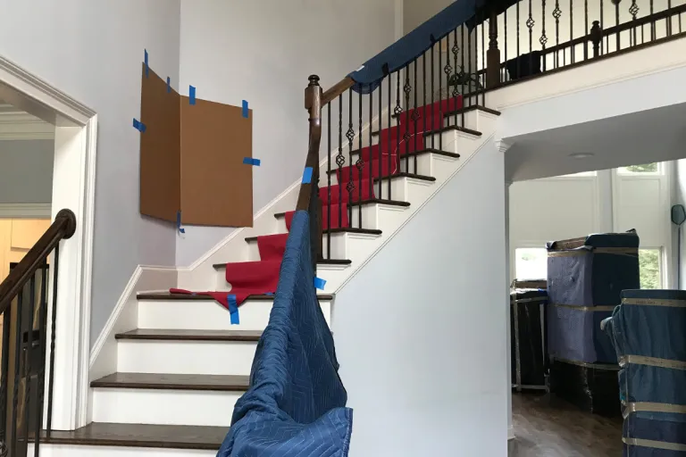 Interior staircase with red carpeted steps, a blue blanket draped over the railing, and a cardboard panel taped to the wall.