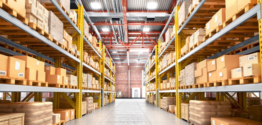 A spacious warehouse interior with tall shelves filled with cardboard boxes, organized along a wide aisle leading to a door.